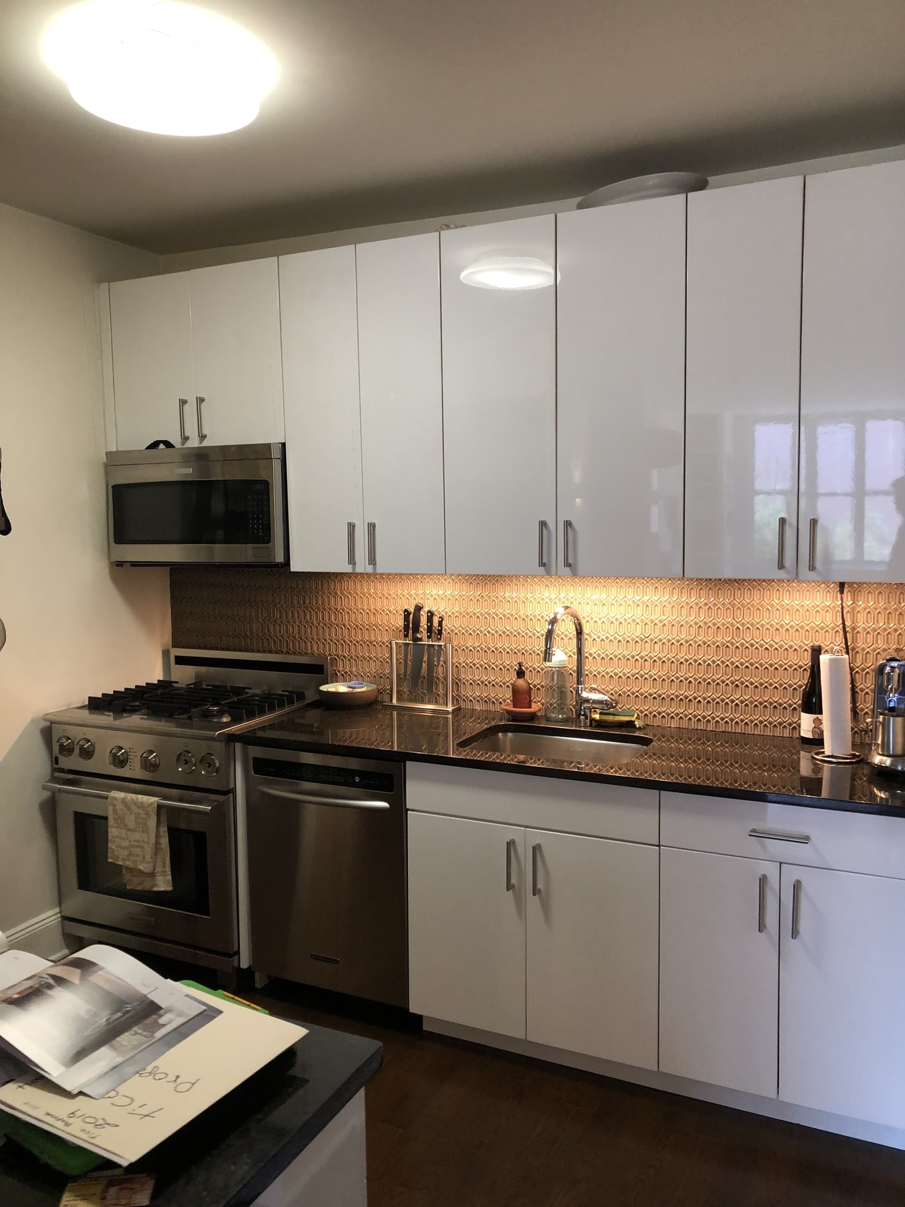 Uptown Manhattan kitchen renovation with high-gloss white cabinetry, copper geometric tile backsplash, and stainless steel appliances — FF Solutions