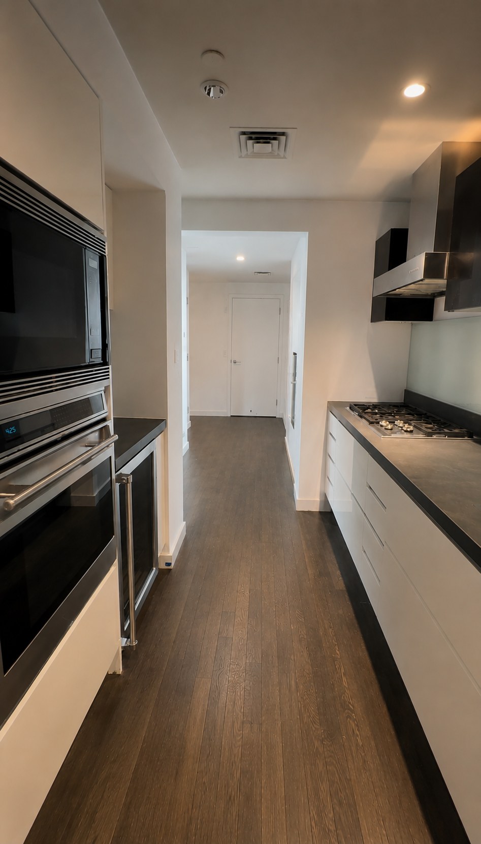 Modern galley kitchen renovation with dark hardwood floors, stainless steel appliances, and white cabinetry in a New York City apartment